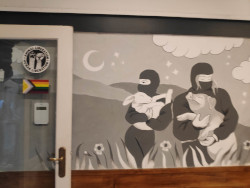 An LGBTQ+ sticker, an animal liberation sticker, and a painting on the wall of two ninja-like activists holding a happy lamb and a happy pig.
