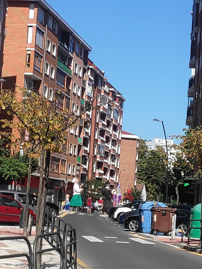 A street with a giant puppet in the distance. The puppet seems to be dressed in traditional women's clothes.