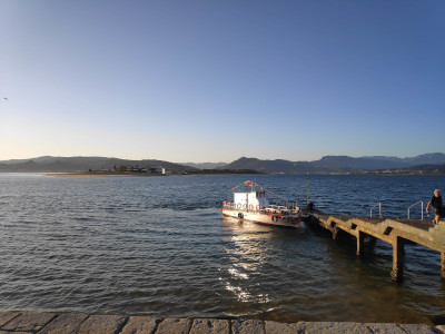 Small engine-driven boat tied to a wooden walkway. Mostly white. Several lifebuoys hanging from the boat's railing. And some bunting.