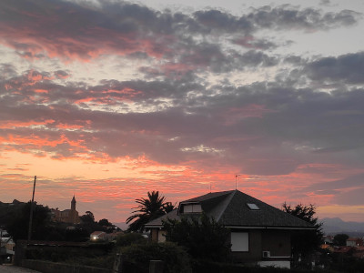 A very red sky, looks like a painting, lots of grey-blue clouds. A church in the background, a house in the foreground.