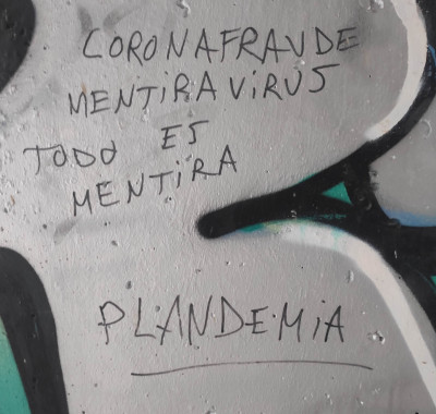 Graffiti on a concrete wall. It says 'coronafraude, mentiravirus, todo es mentira, plandemia'.