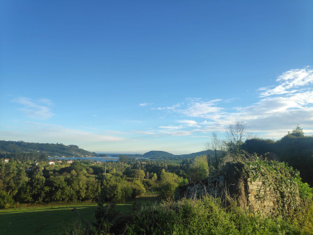 A poorly framed picture of Spanish countryside with the sea and towns in the background and overgrown ruins in the foreground.