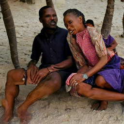 A Black family sitting on a beach under some palm trees, their faces are quite messed up and their bodies are disconnected / intersecting with the trees.